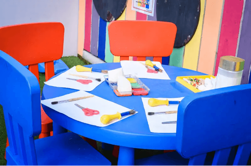 Children's art table with blue chairs, art supplies, and paper for creative activities
