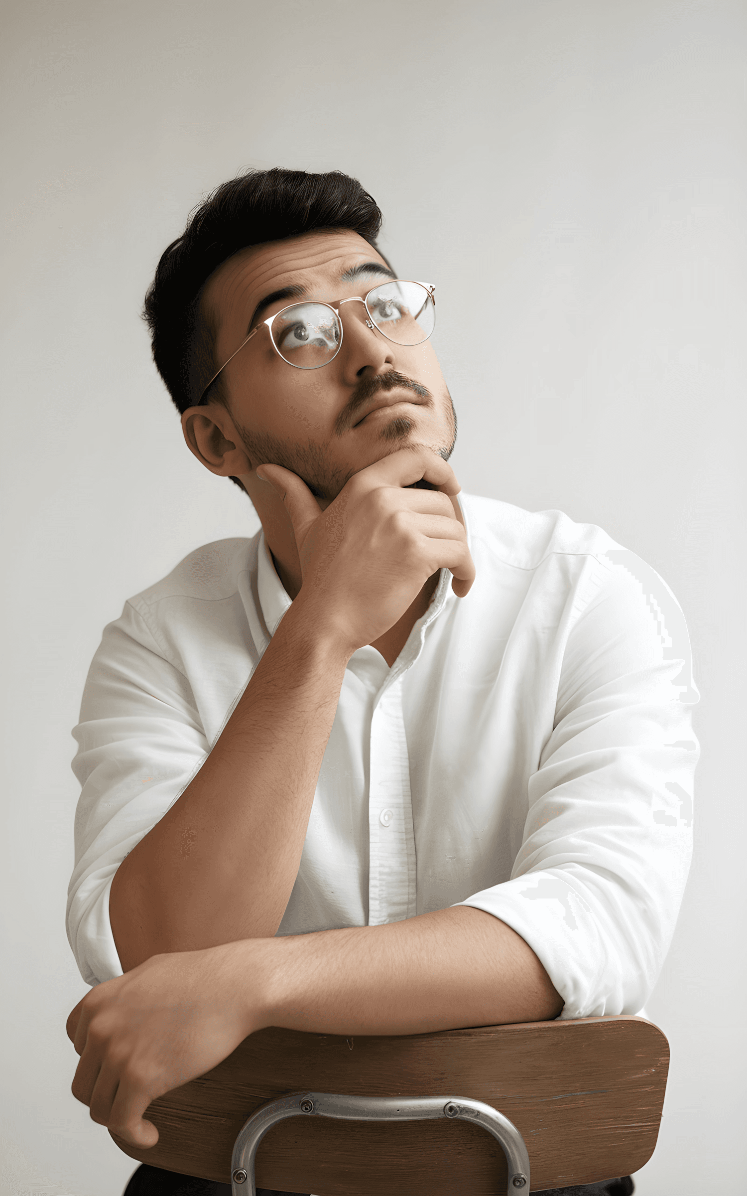 Thoughtful young man in a white shirt and glasses against a plain background.