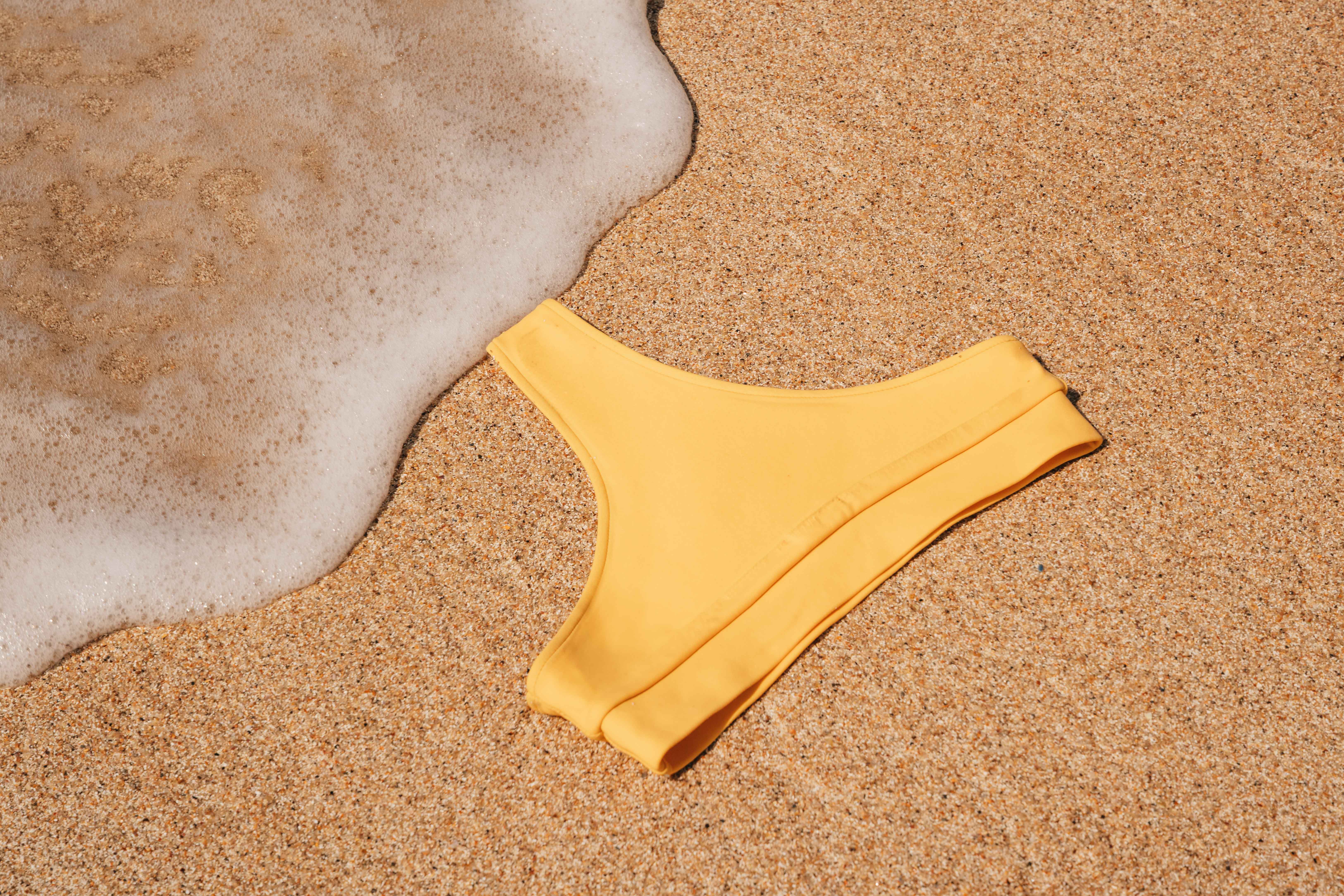 Yello bikini pants laying on the sand with wave foam next to it
