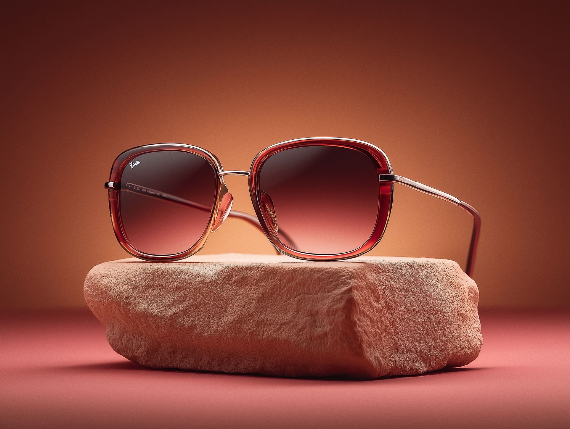 Rose gold oversized sunglasses resting on natural stone against coral pink backdrop