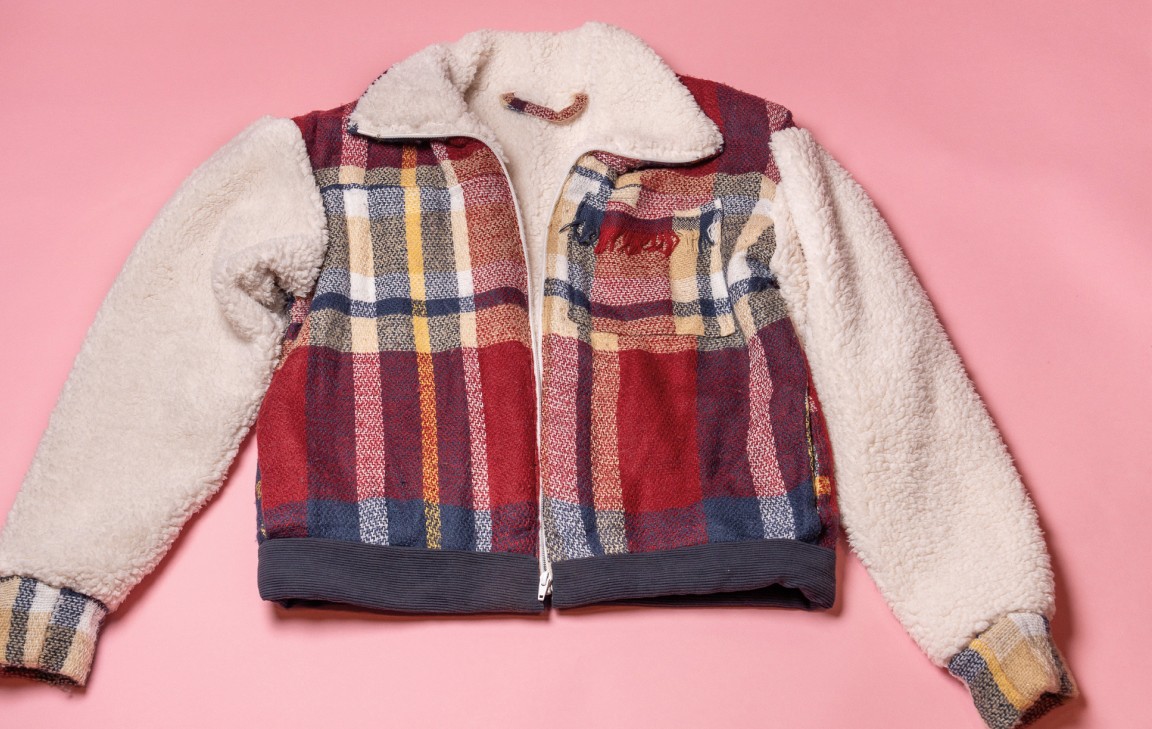 Patchwork jacket with plaid panels and a sherpa collar photographed against a pink background.