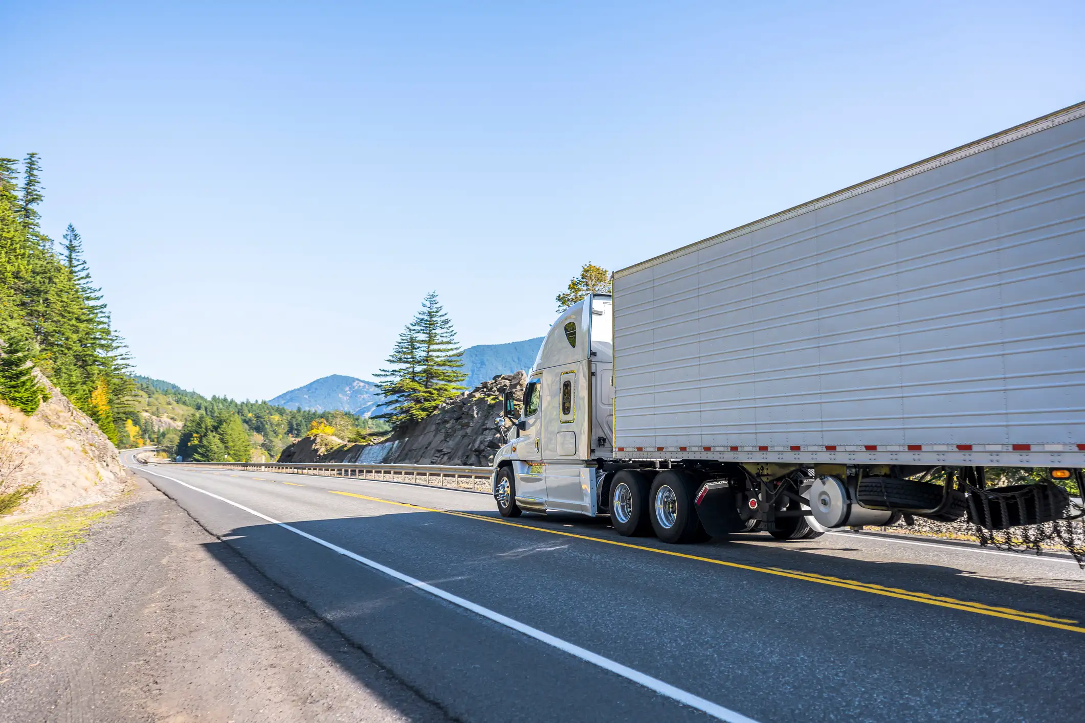 White semi-truck hauling a trailer through a mountain highway — used on the GIA Group, LLC New in Business Guide page to represent new trucking companies starting operations.