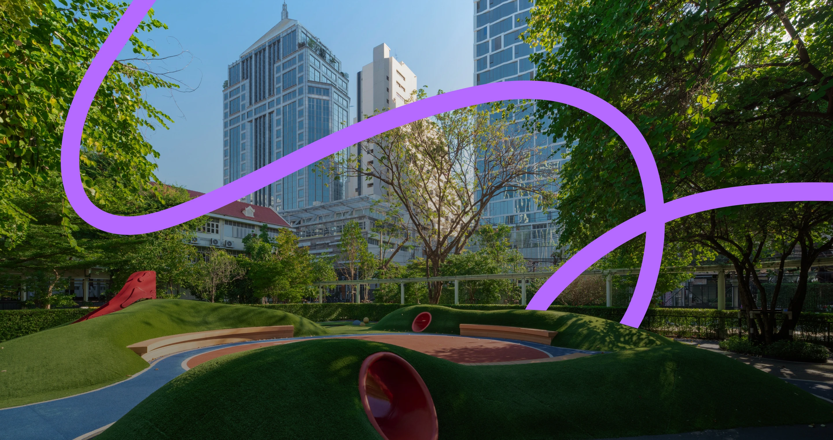 A modern playground with grassy mounds and red tunnels is surrounded by tall buildings and lush green trees, under a clear blue sky with a purple ribbon design.