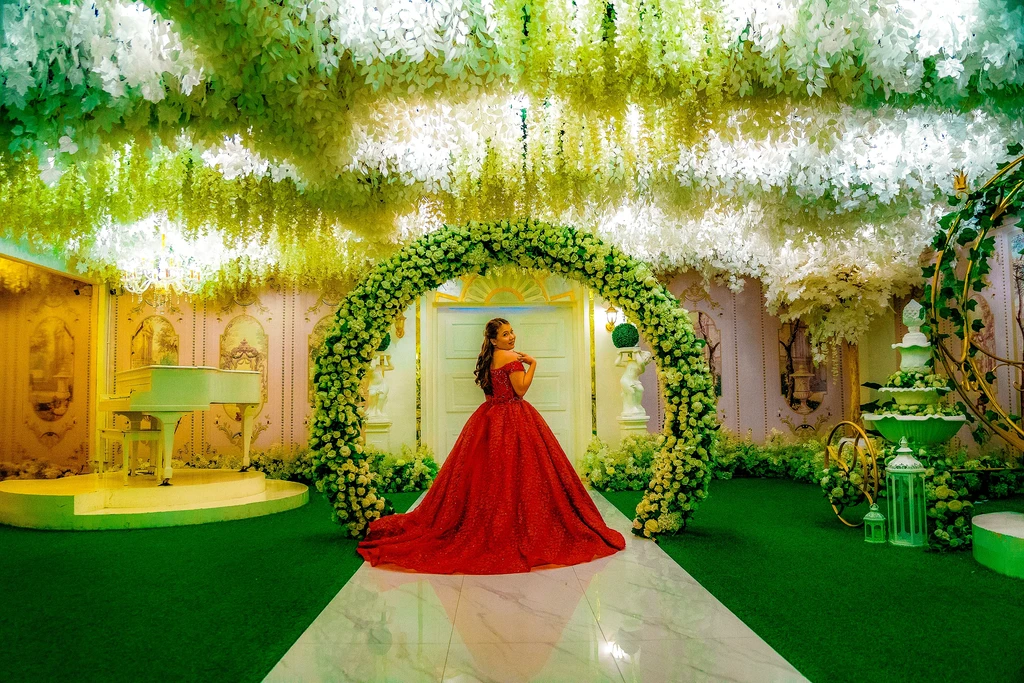 Debutante in a red gown under the white floral arch at Celestia Hall, Quezon City