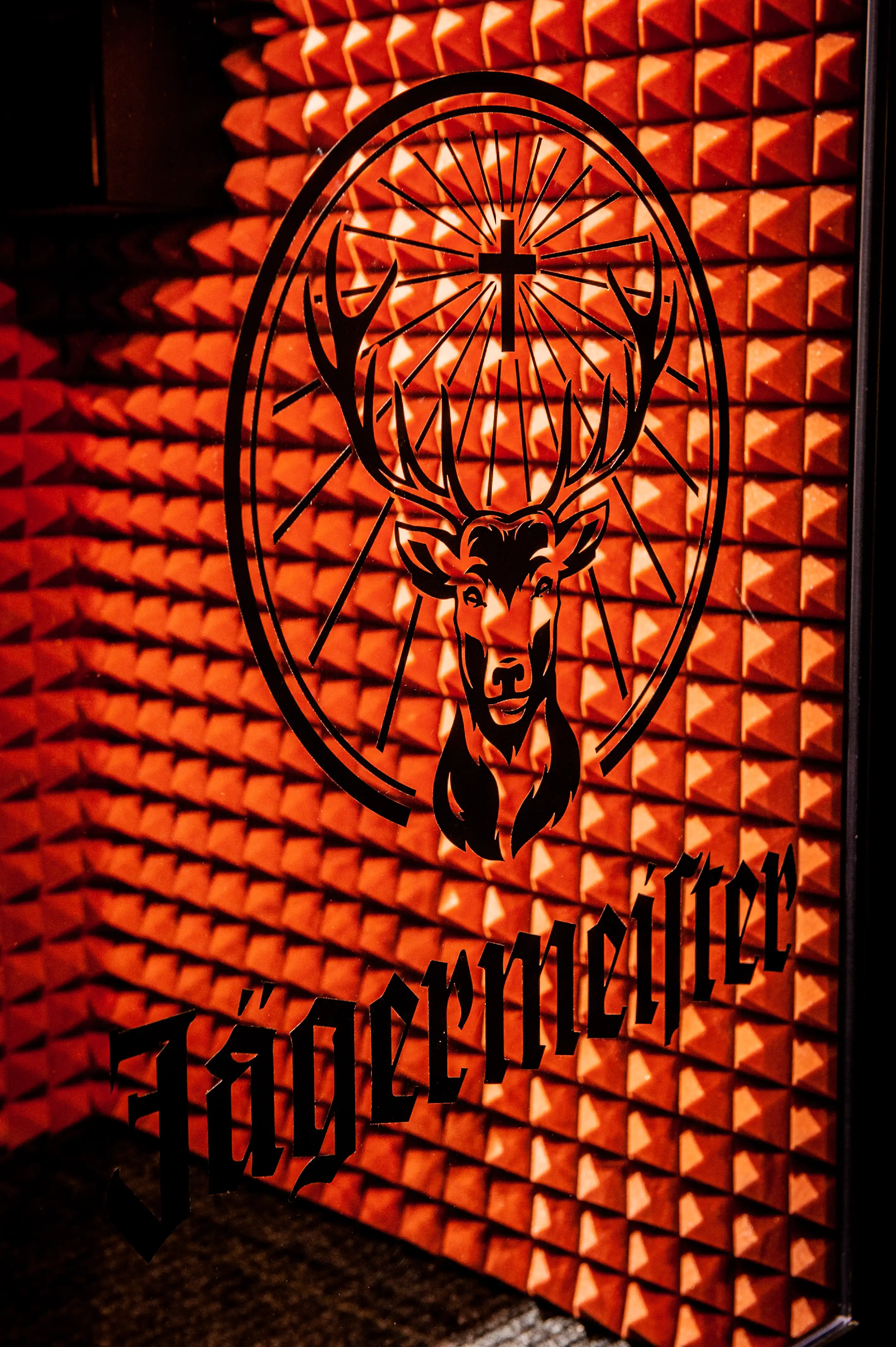 Jägermeister stag logo printed on an orange-lit wall of pyramid acoustic foam at JÄGERMEISTER x SVENNI'S with black gothic lettering below.