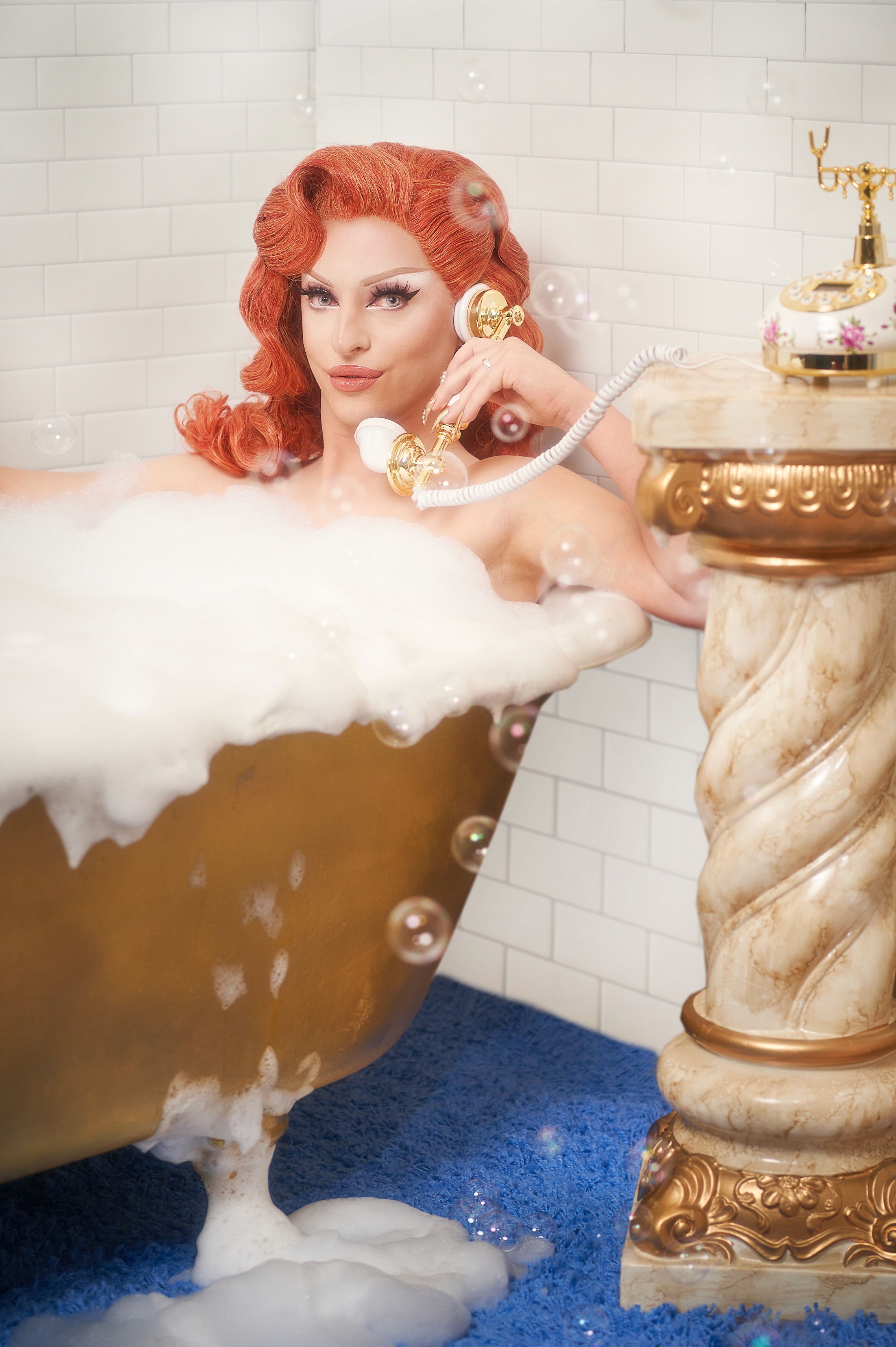 Miz Cracker holding a vintage telephone in an ornate gold bathtub