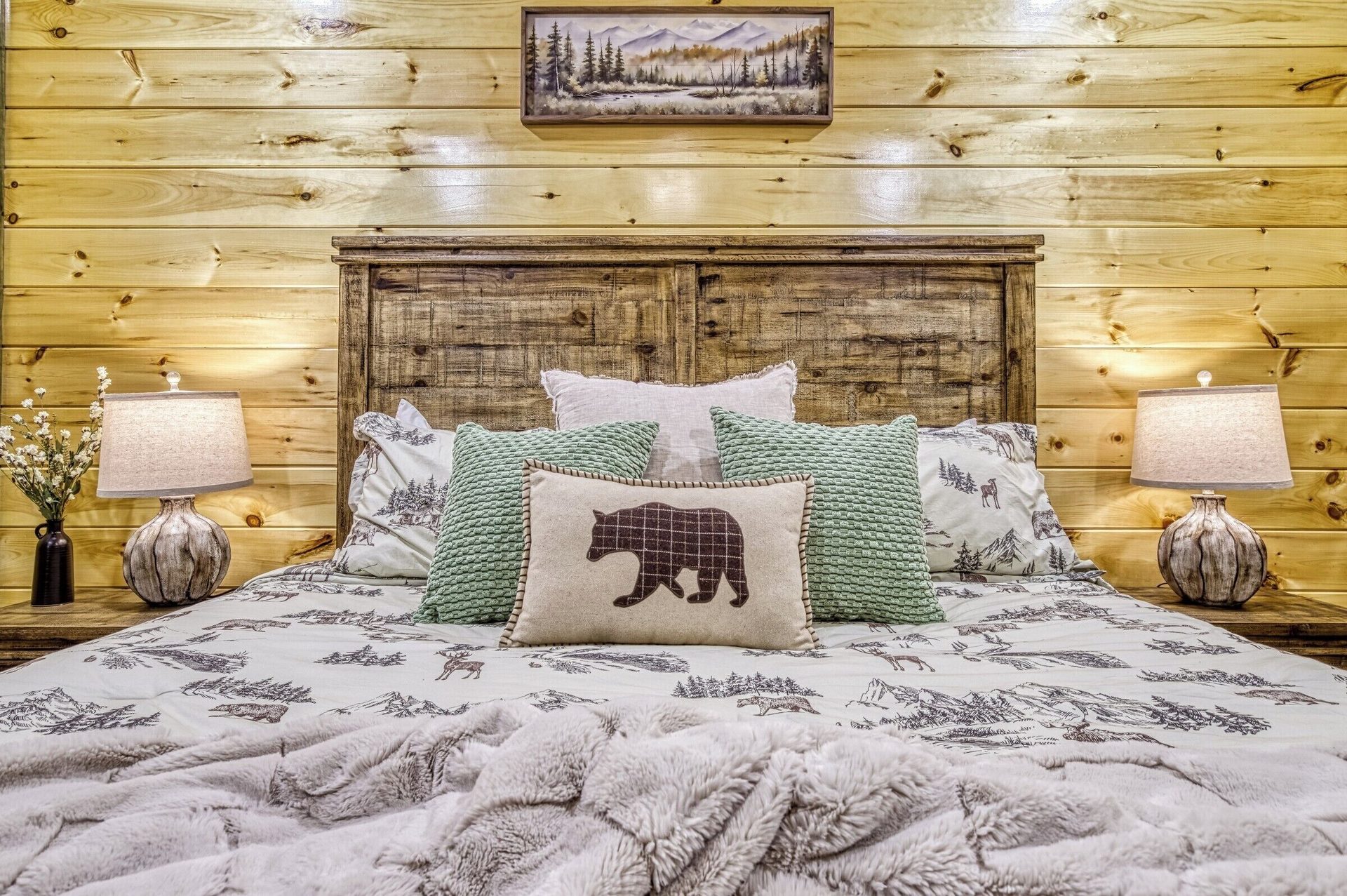 King bed with rustic wood headboard, white pine-print bedding, bear pillow and lamps