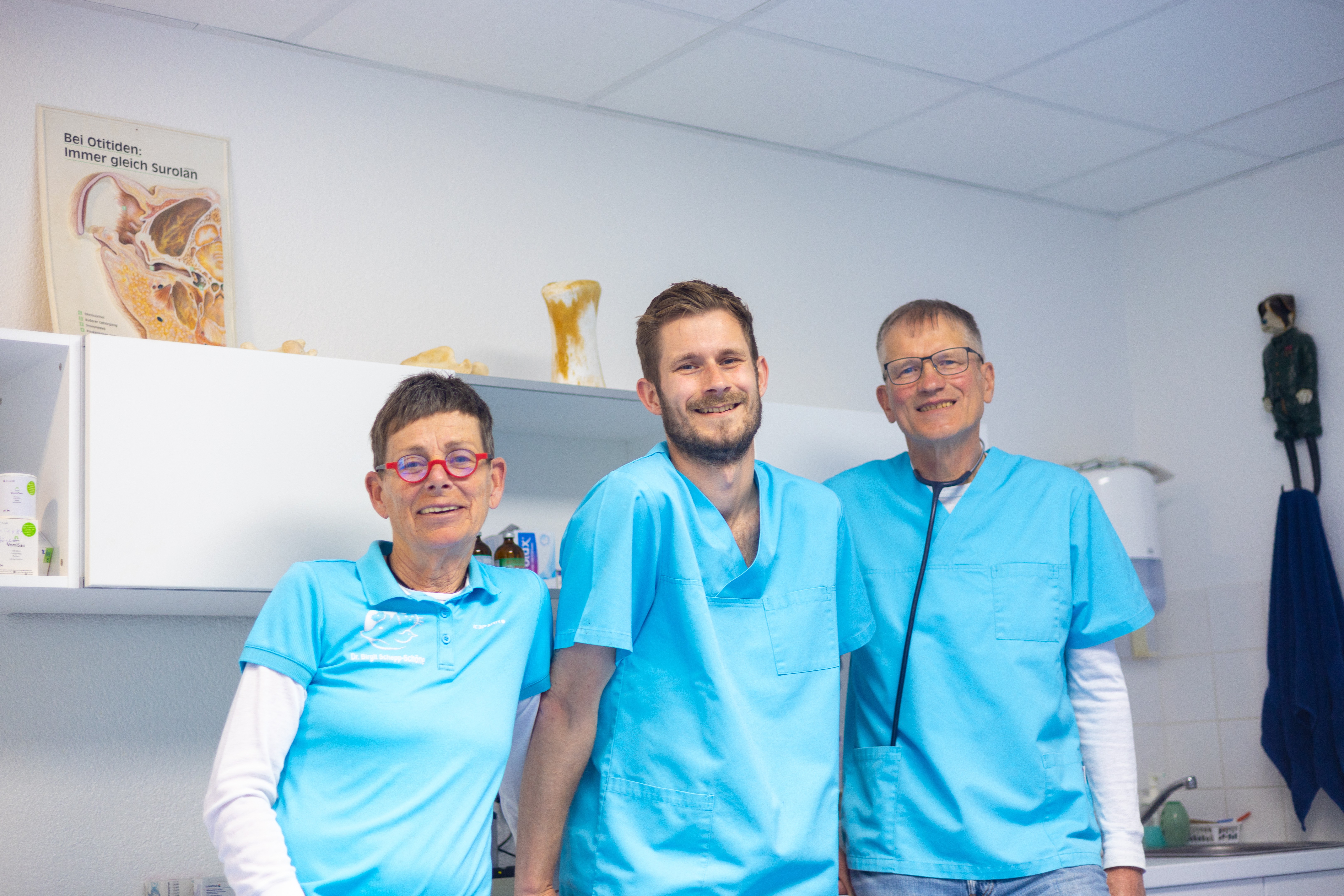 Drei Tierärzte lächeln in einer Tierarztpraxis. Sie tragen blaue Arbeitskleidung.