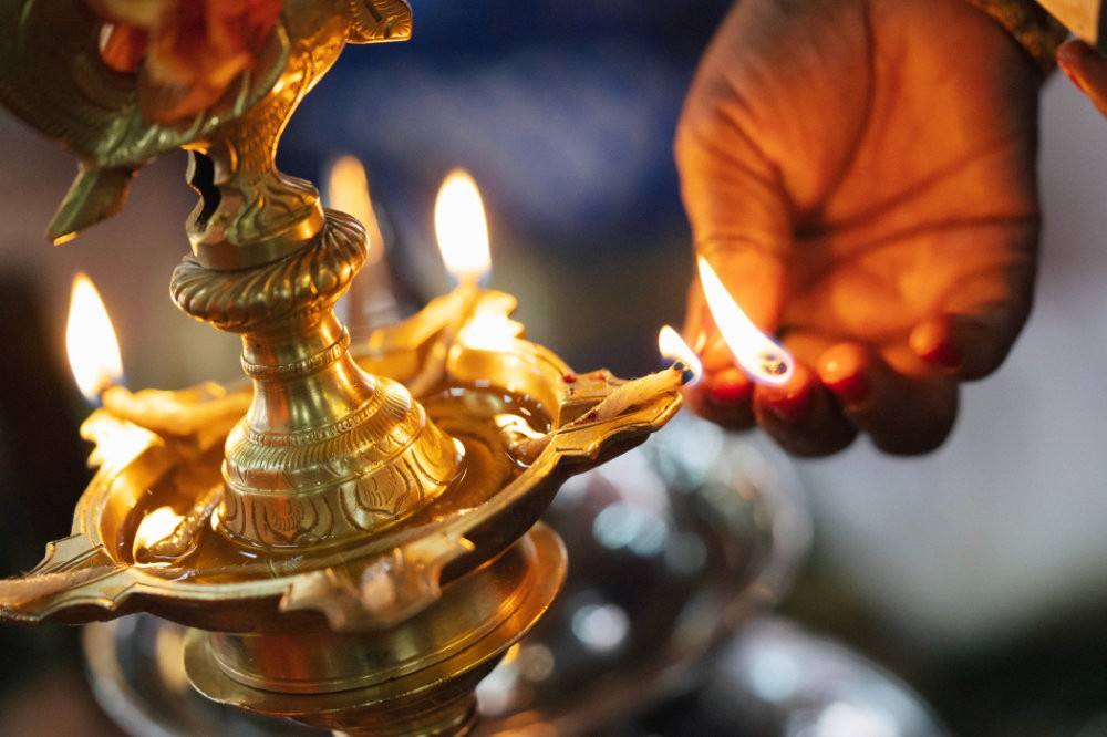 A hand lighting an oil lamp, surrounded by flickering flames, set against a softly blurred background.
