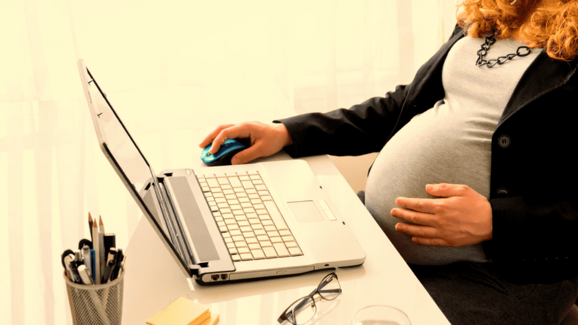a pregnant lady touches her pregnant belly, while working on her laptop computer