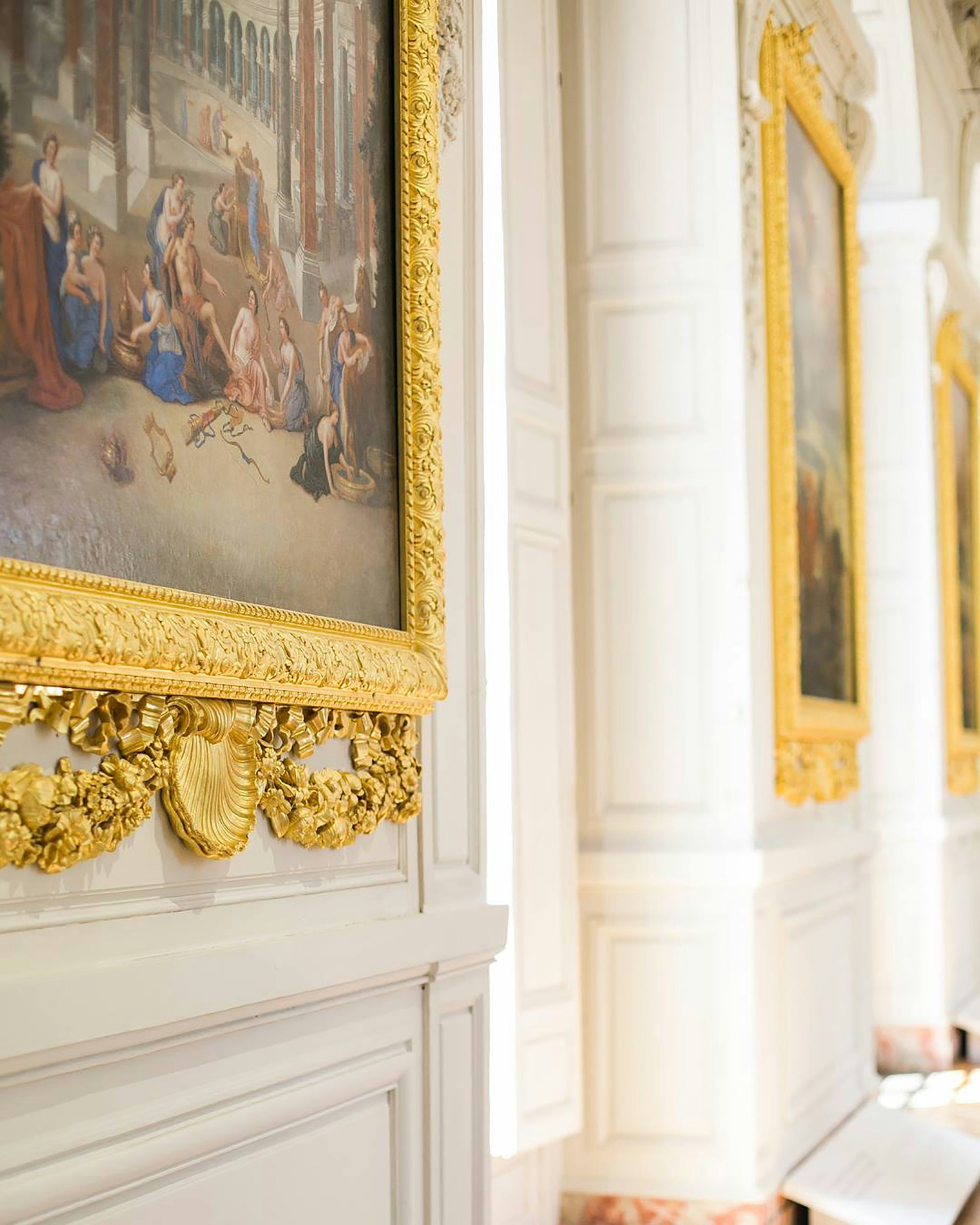 Ornate gold-framed classical paintings displayed along a white gallery wall in a museum setting.