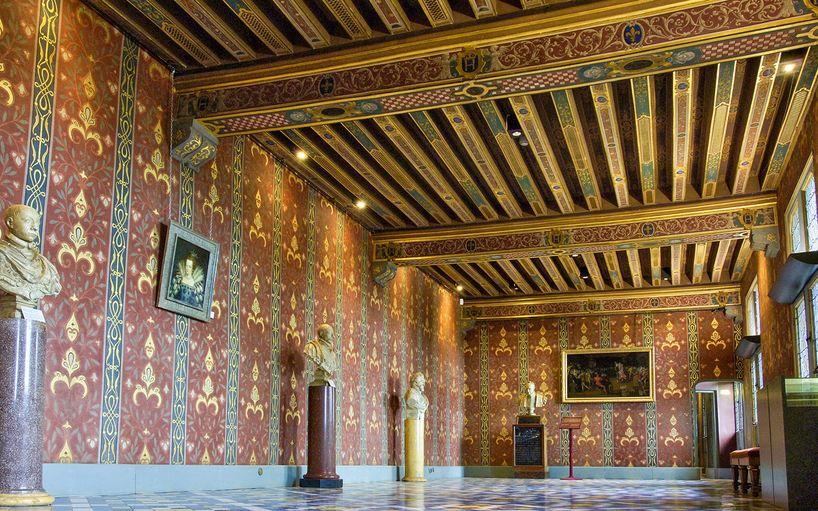 Интериорът на замъка Роял Блоа с богато украсени червени и златни стени, декоративен таван и скулптури.