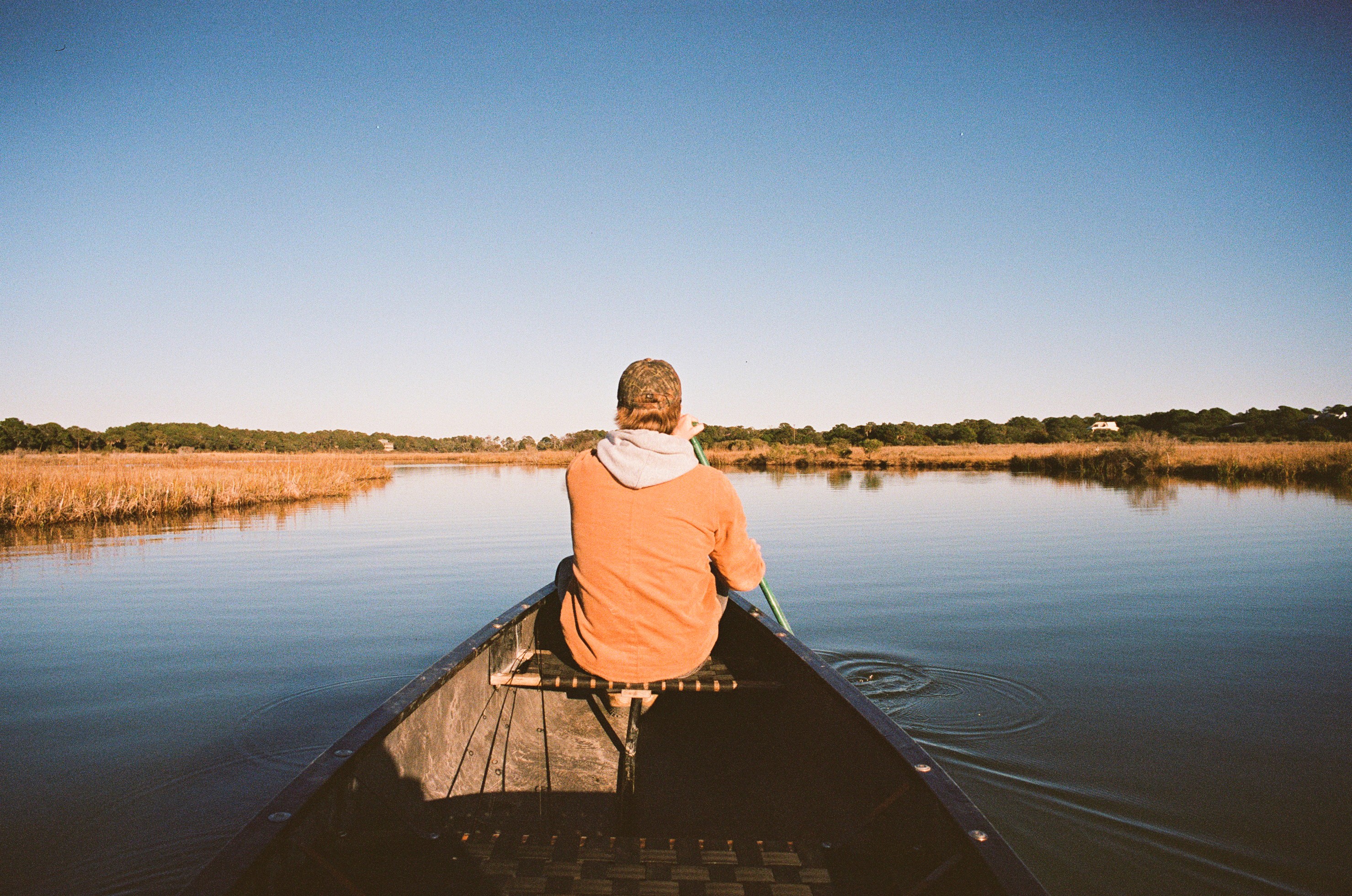 Person sitting quietly in a canoe on calm water, facing an open horizon.