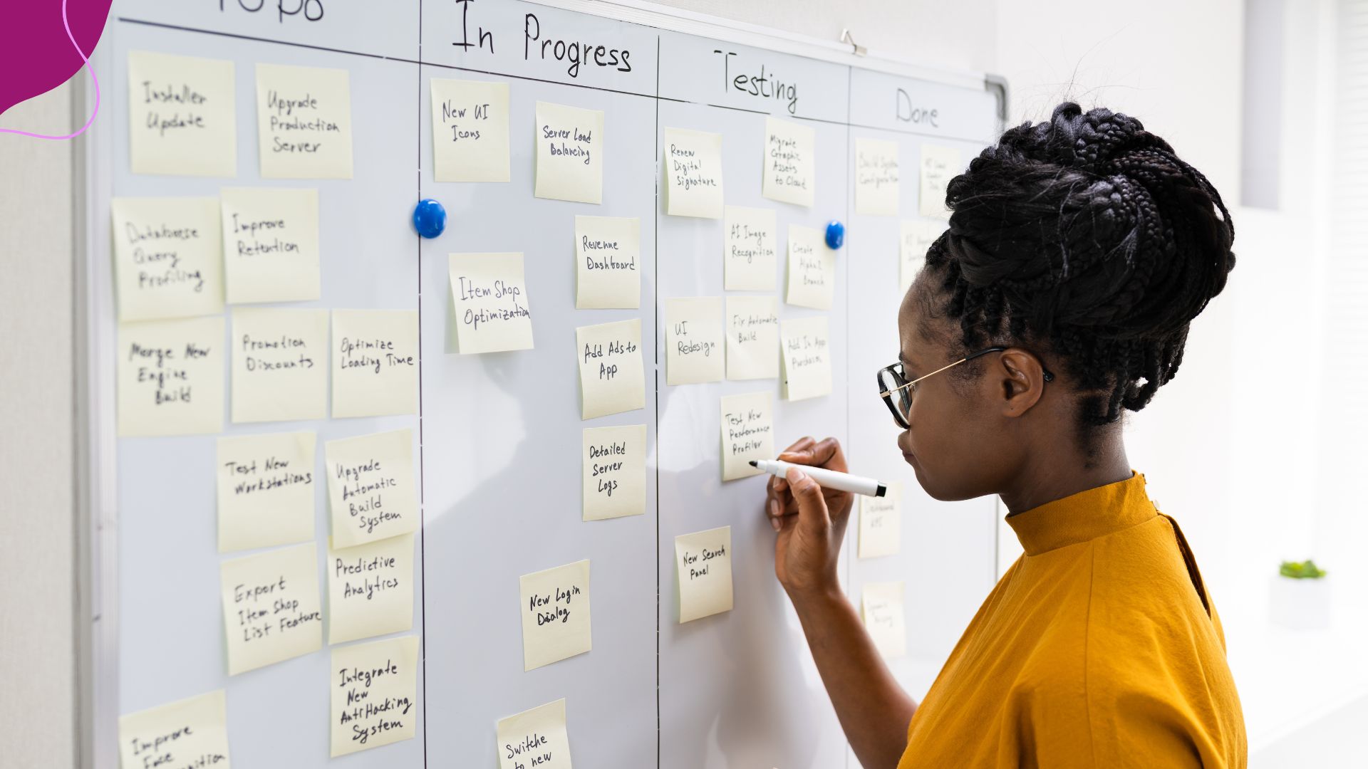 black woman in yello shirt writing on poste-it notes anhearded to a whiteboard