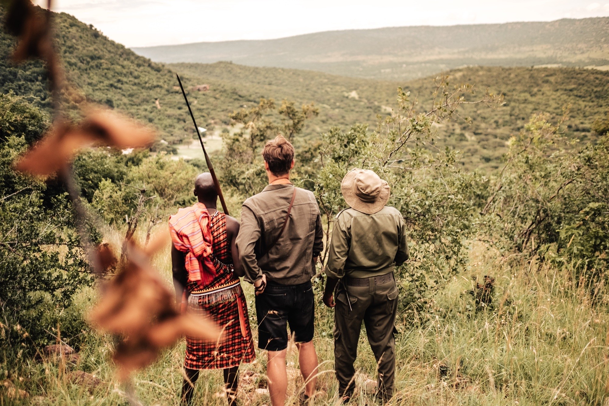 A Maasai guide and a field guide leading a guest on foot above wooded hills