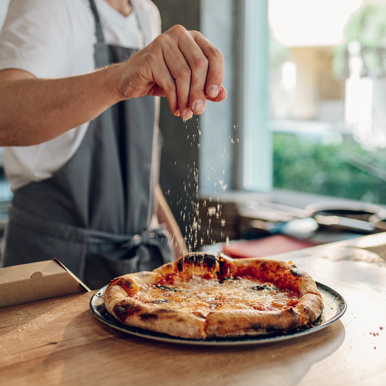 Photo of a pizza and chef sprinkling cheese.
