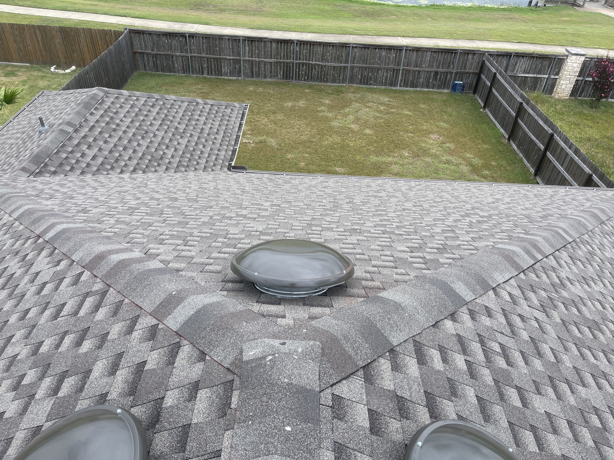 A round roof vent near intersecting shingle roof slopes. A photo cannot establish the vent’s rated airflow.