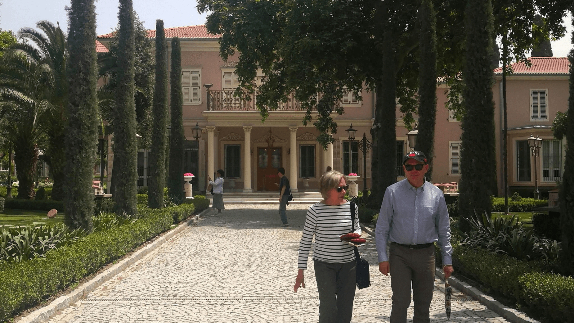 Visitors walking through the gardens of a historic mansion in Istanbul, elegant estate surrounded by tall trees, landscaped pathways, and classic architecture