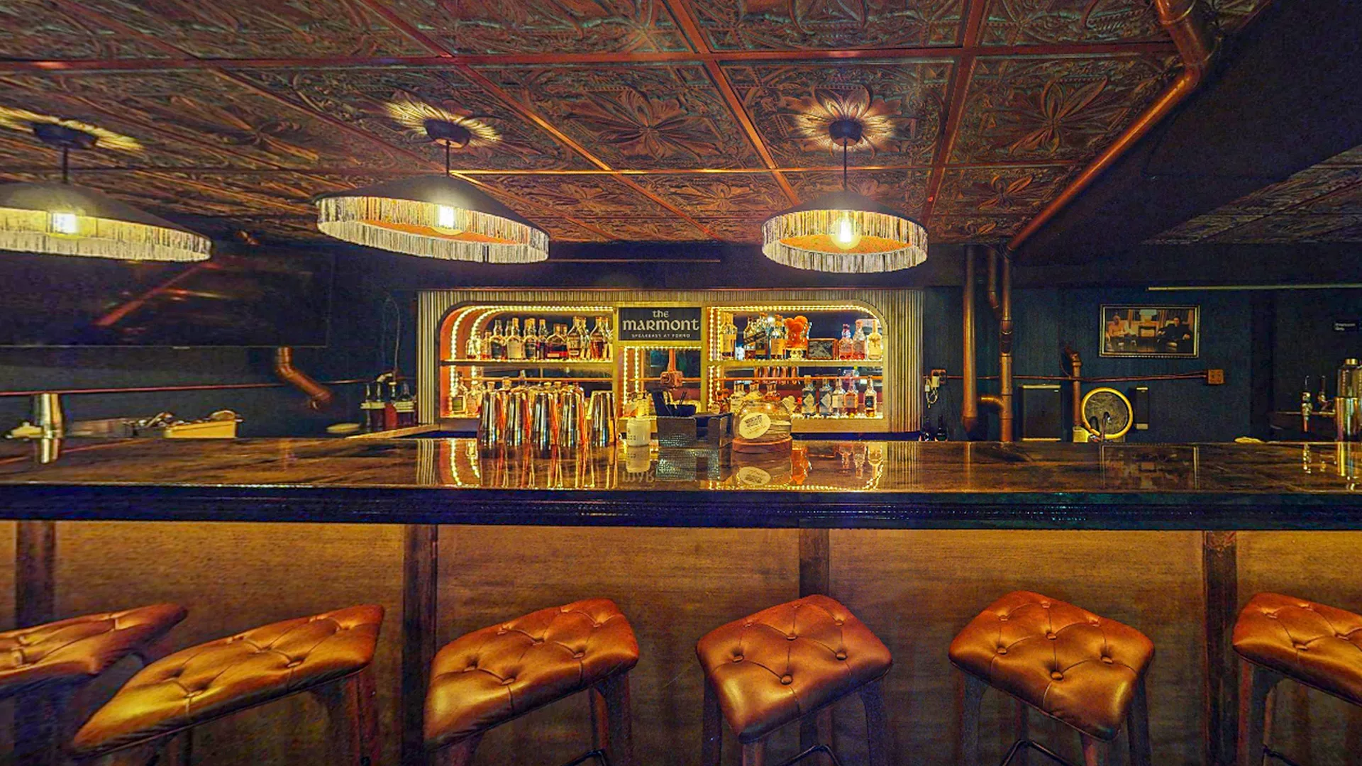 Bar with tufted leather stools, a tin ceiling and pendant lights at Forno Kitchen + Bar