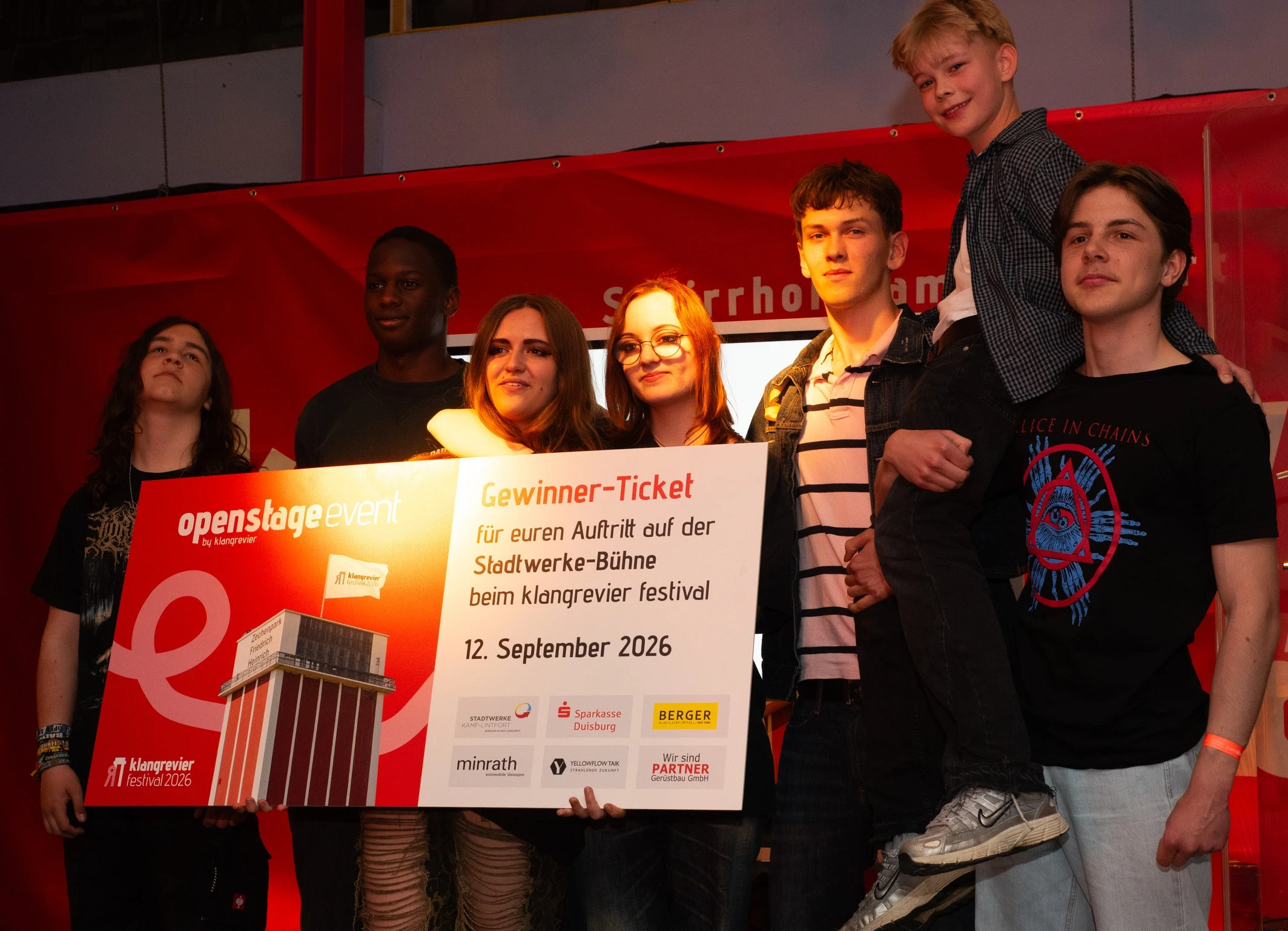 Gewinnerband Teenage Bedlam steht nach der klangrevier openstage 2026 mit dem Gewinner-Ticket für ihren Auftritt auf der Stadtwerke-Bühne beim klangrevier festival am 12. September 2026 vor rotem Bühnenhintergrund.