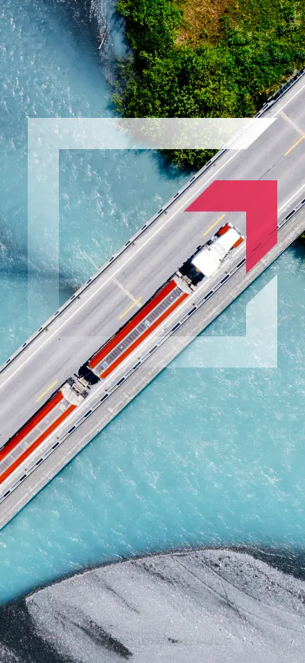 Aerial view of a semi-truck driving across a bridge over blue water representing commercial truck insurance services by GIA Group, LLC