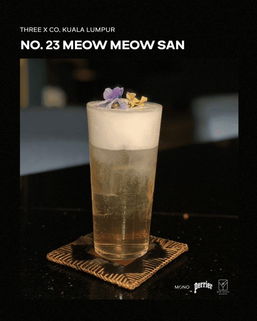 A cocktail named 'Meow Meow San' from Three X Co, Kuala Lumpur, presented in a glass with floral garnishes, placed on a decorative coaster.