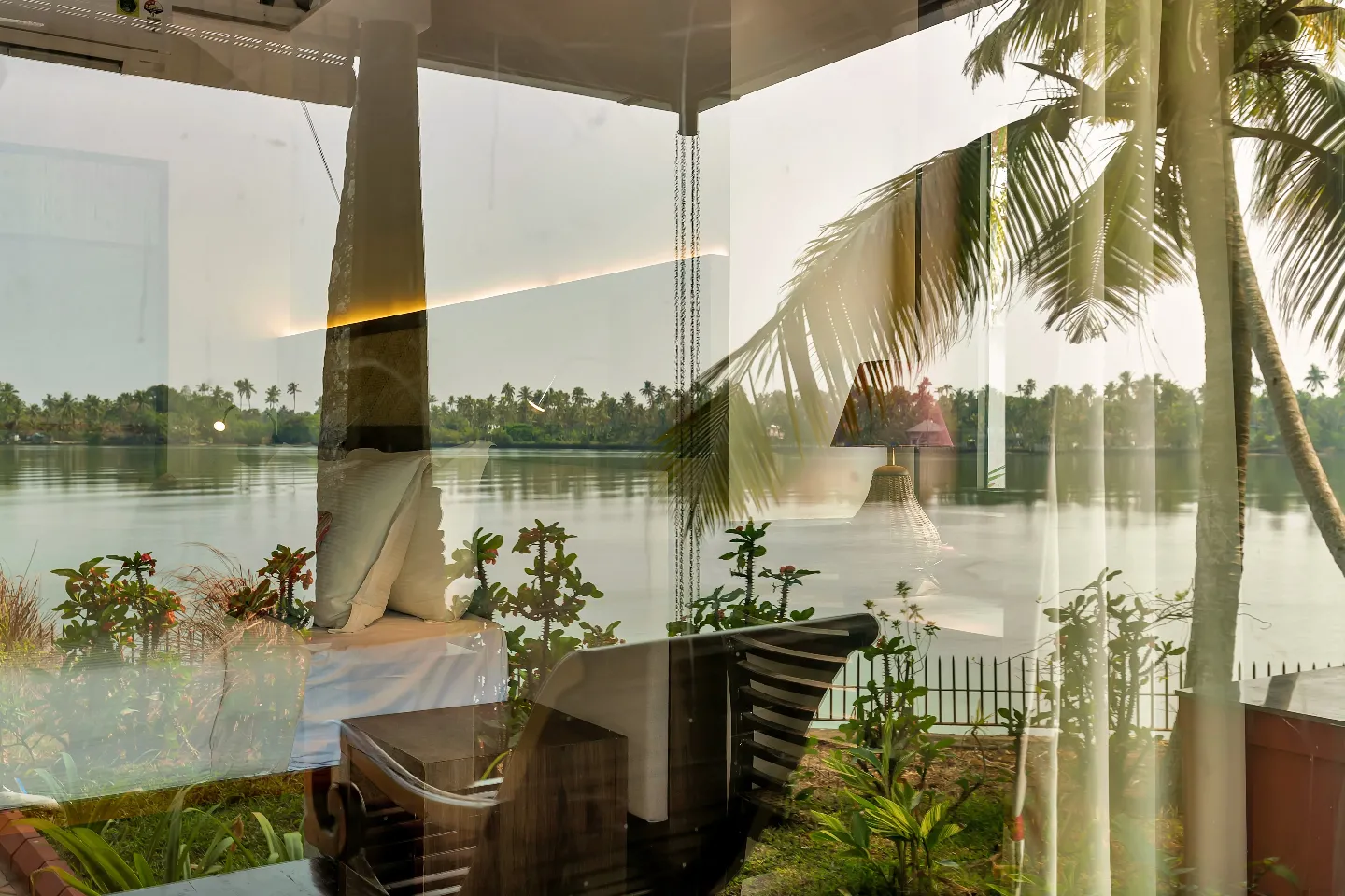Lake View Villa bedroom at Vedic Village Kodungallur with a king bed, writing desk and floor-to-ceiling window overlooking the lake and coconut palms