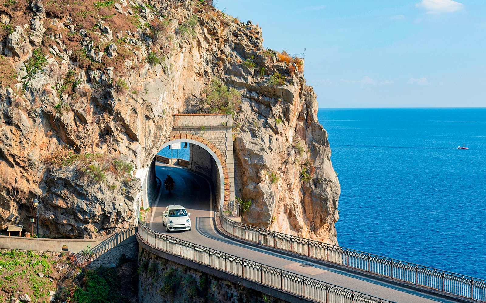 Car driving through a coastal tunnel on the Amalfi Coast with sea views.