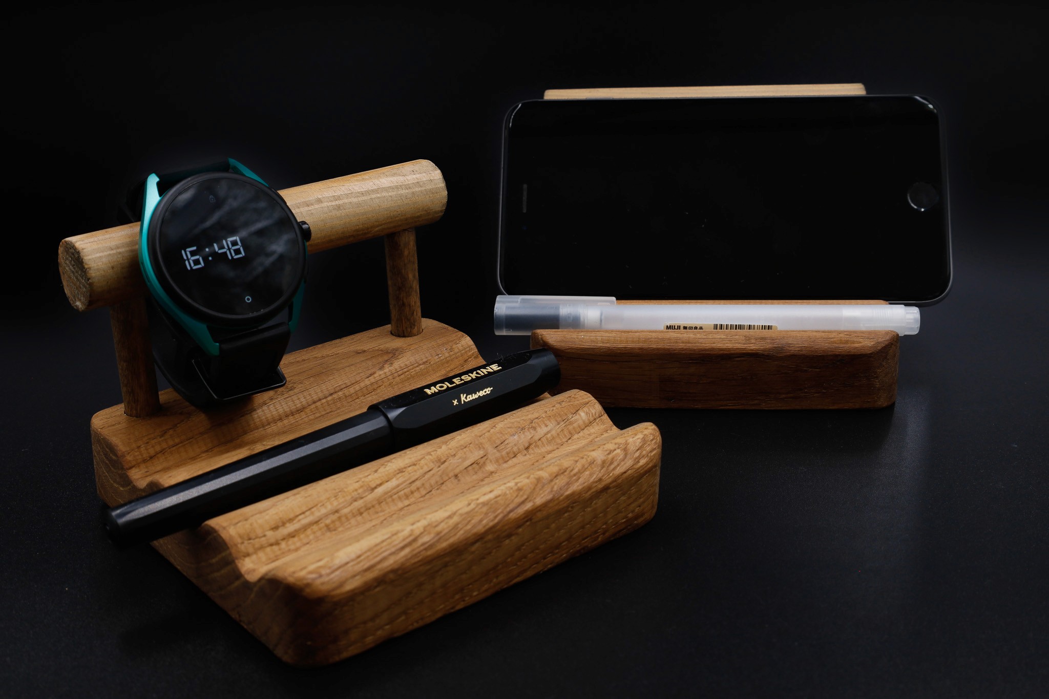 Elegantly organized modern gadgets: a wristwatch, smartphone, and pen rest on a stylish wooden stand against a dark backdrop