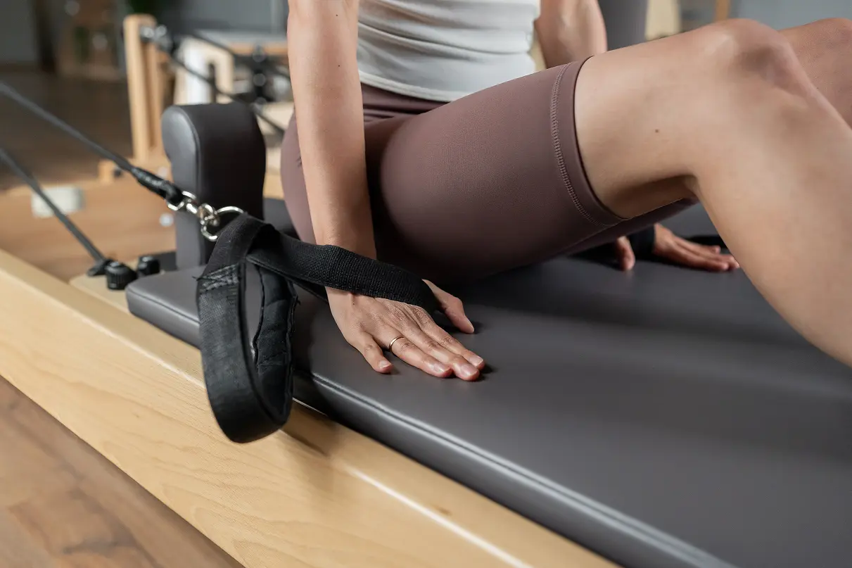 woman sitting on reformer machine with a focus on her legs, forearms and hands