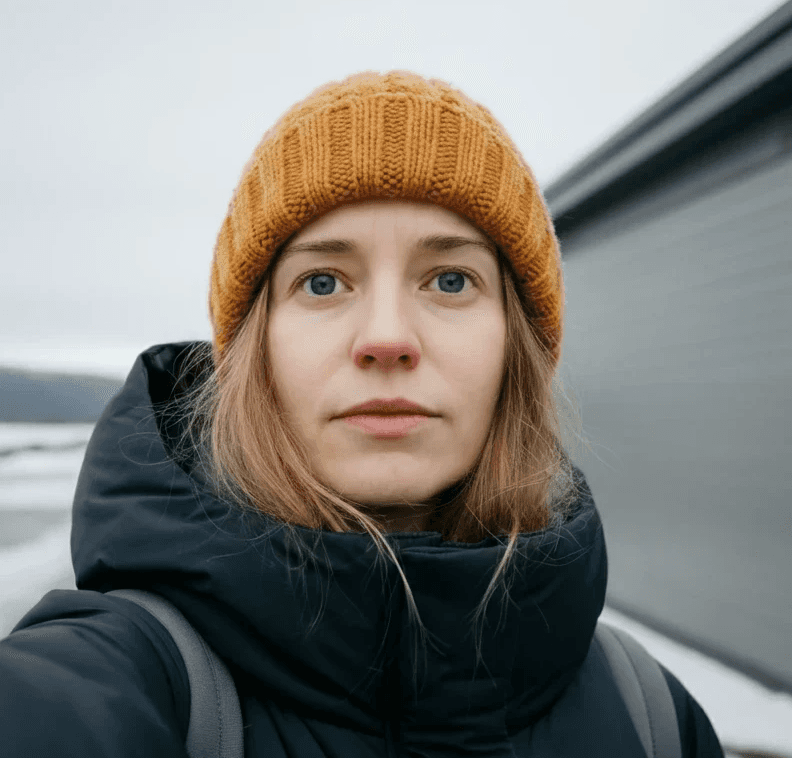 A fair-skinned woman with blonde hair, blue eyes, and wearing an orange beanie and a black jacket.