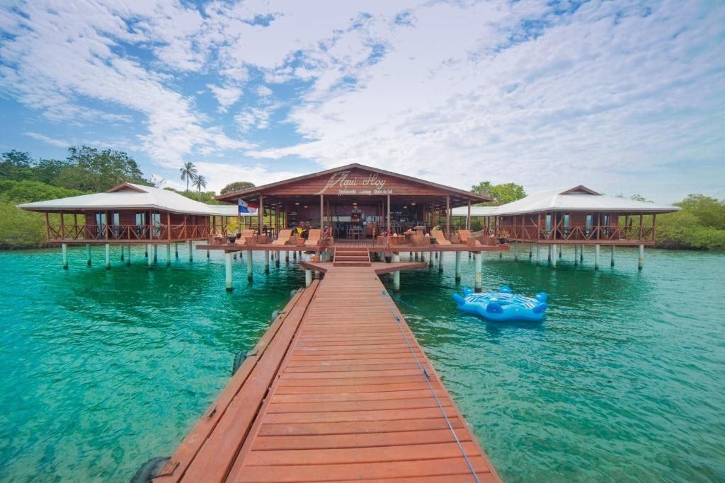 Wooden dock leading to overwater bungalows above clear turquoise water.