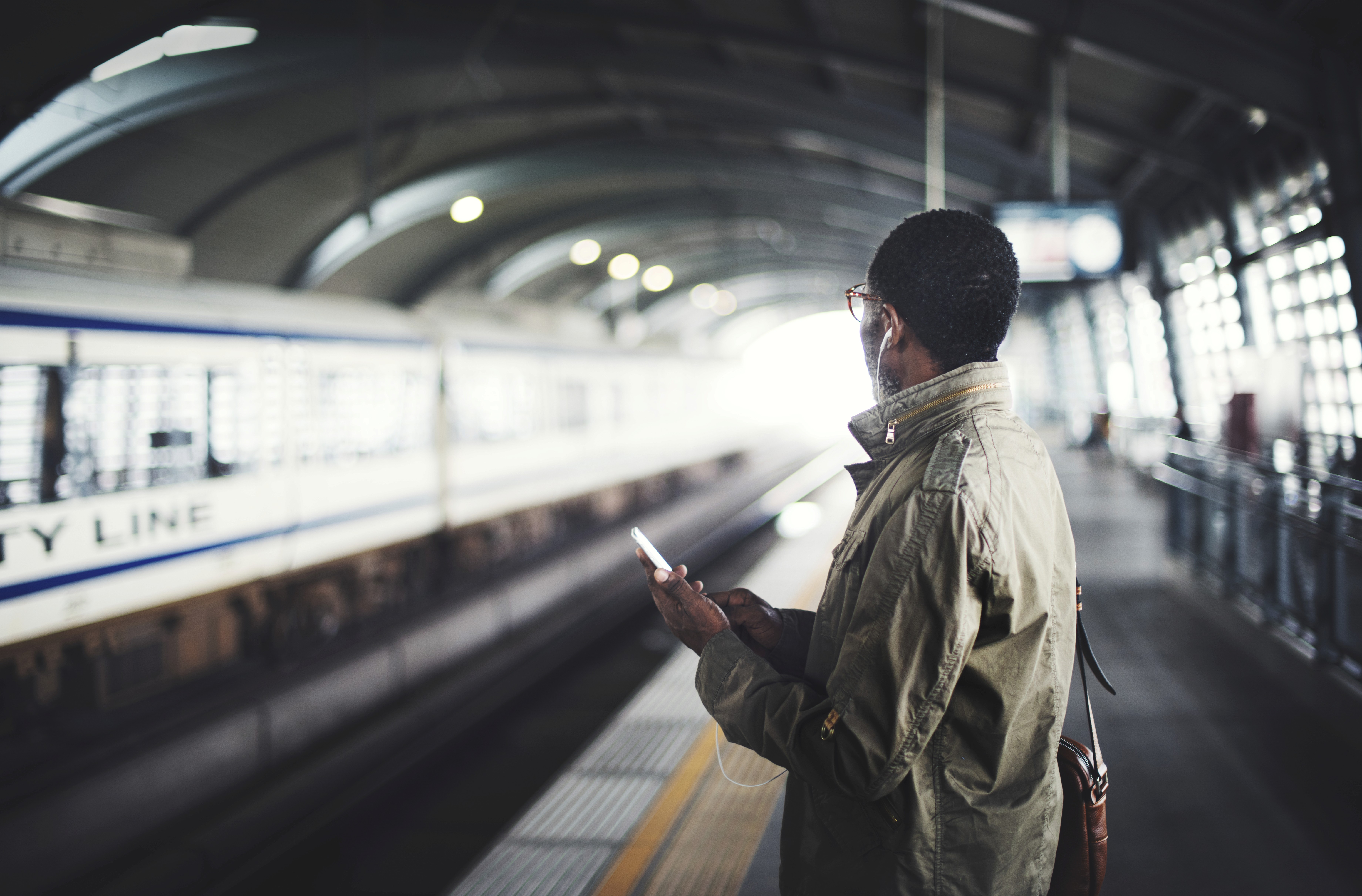 Person holding a phone while waiting on a train platform as a train passes.