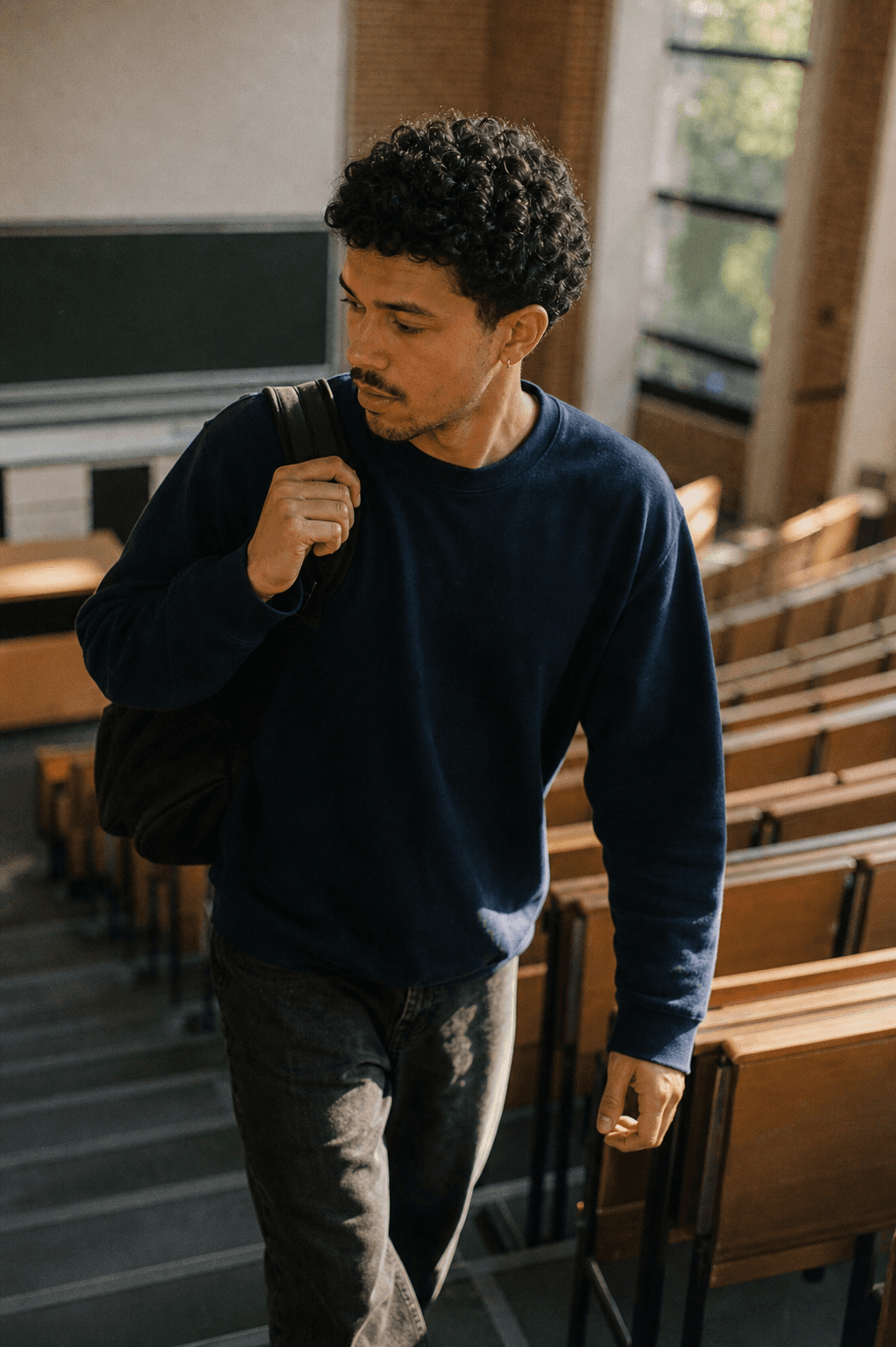 Student walking the steps of an empty lecture hall, backpack on, looking for a seat