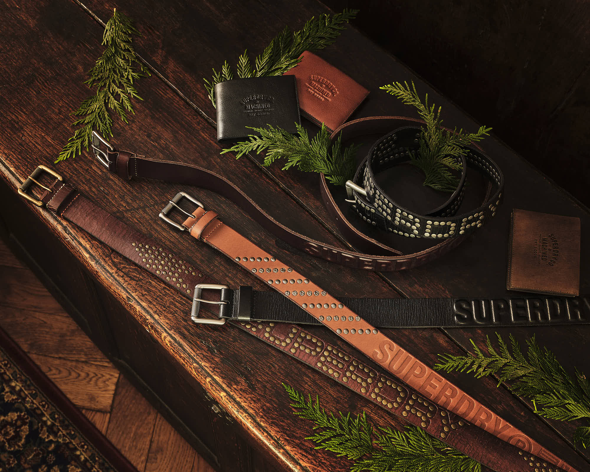 Stylish leather belts and wallets on a wooden surface with green foliage, showcasing fashion accessories elegance.