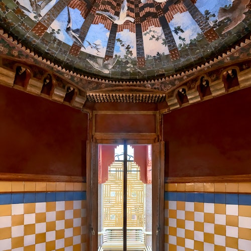 Ozdobny pokój z bogato zdobionym sufitem przedstawiającym ptaki i drzewa, ściany z żółto-białych kafli w szachownicę oraz okno z misterną kratownicą.