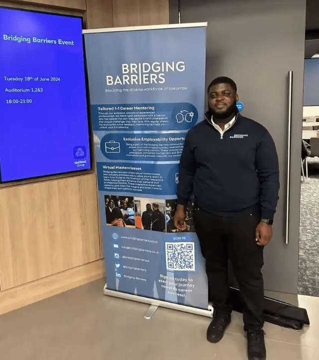 Man standing next to Bridging Barriers navy blue roller banner. 