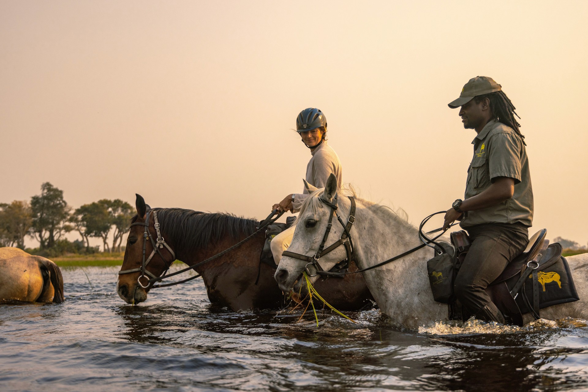 Kujwana Delta Ride, Okavango Delta Botswana. Fem ryttare till häst vadar genom högt vatten i skymning.