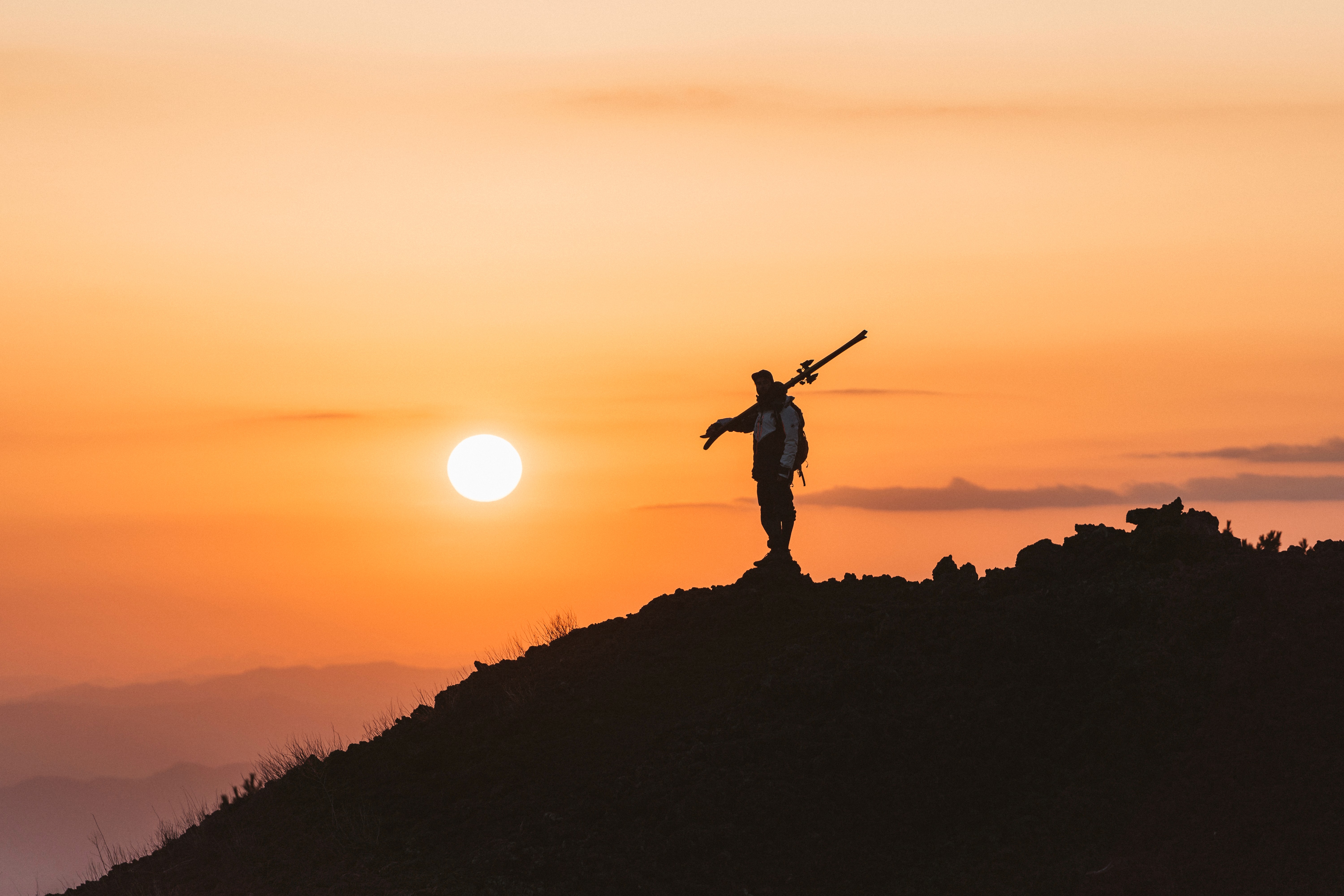 Skier silhouetted on a volcanic ridge at sunset.