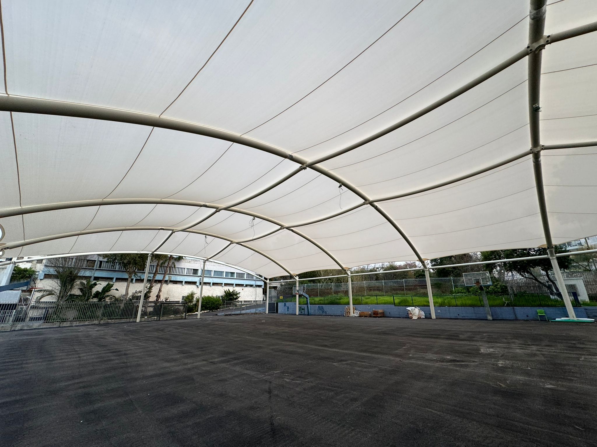Curved beige tent roof with metal frame over a large empty asphalt area.