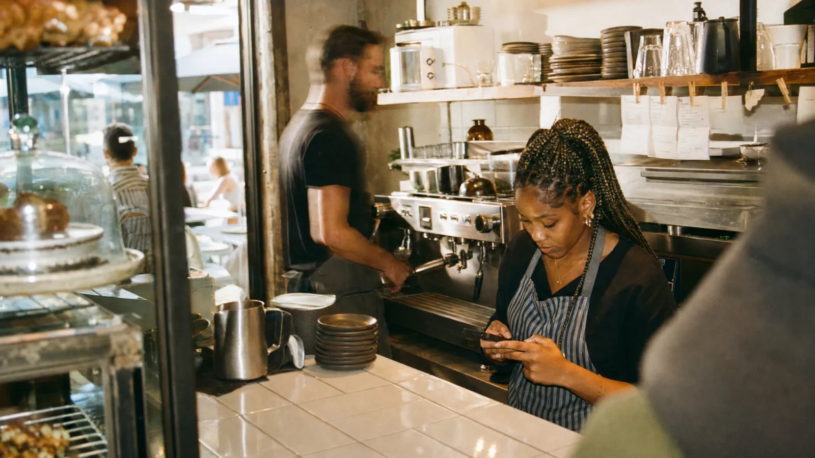Barista risponde a un messaggio sul telefono del locale dietro il bancone tra le comande
