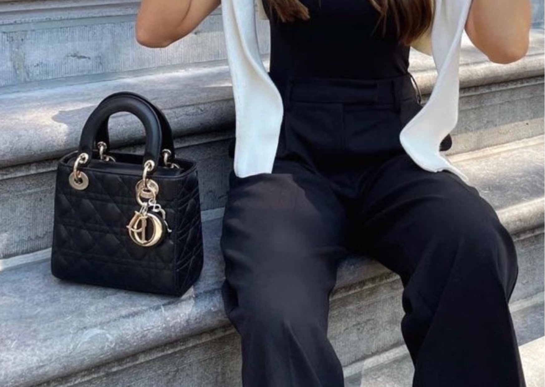 Stylish woman sitting beside the branded, authentic, black, leather Lady Dior bag, outside on the streets.