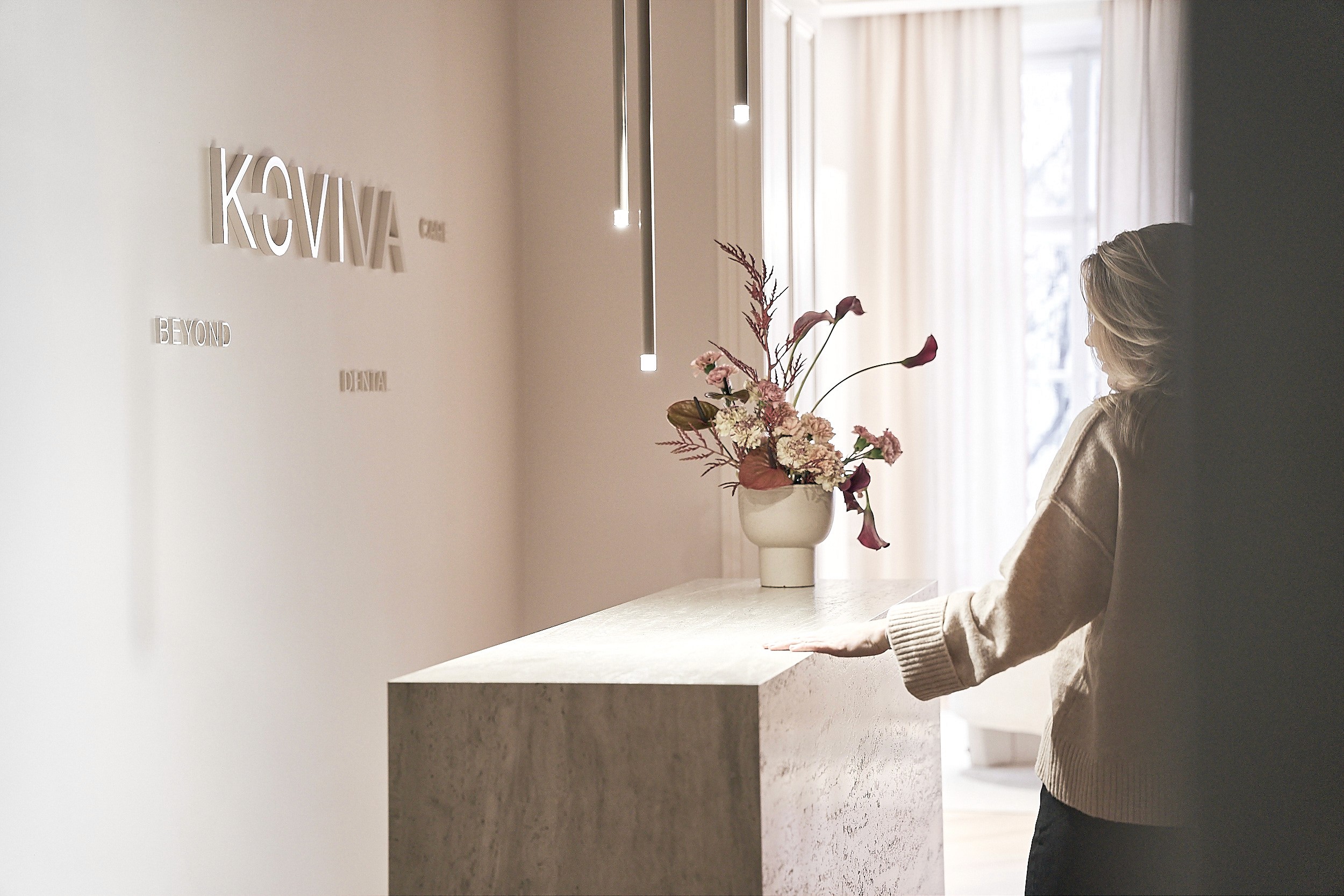 Eine Frau steht an einer Rezeption mit dem Logo "KOVIVA"