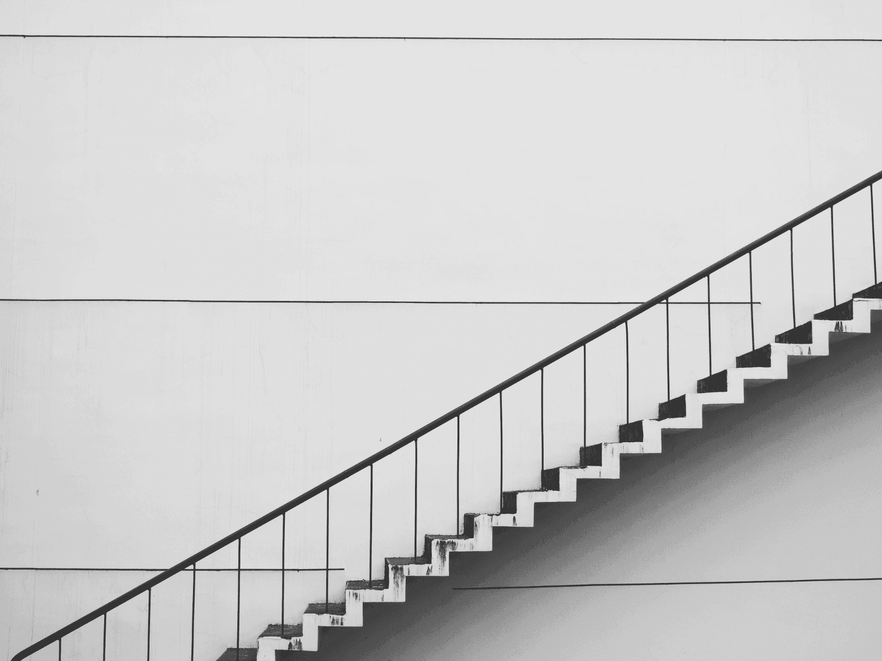 Modern minimalist staircase with black railing against a textured white wall.