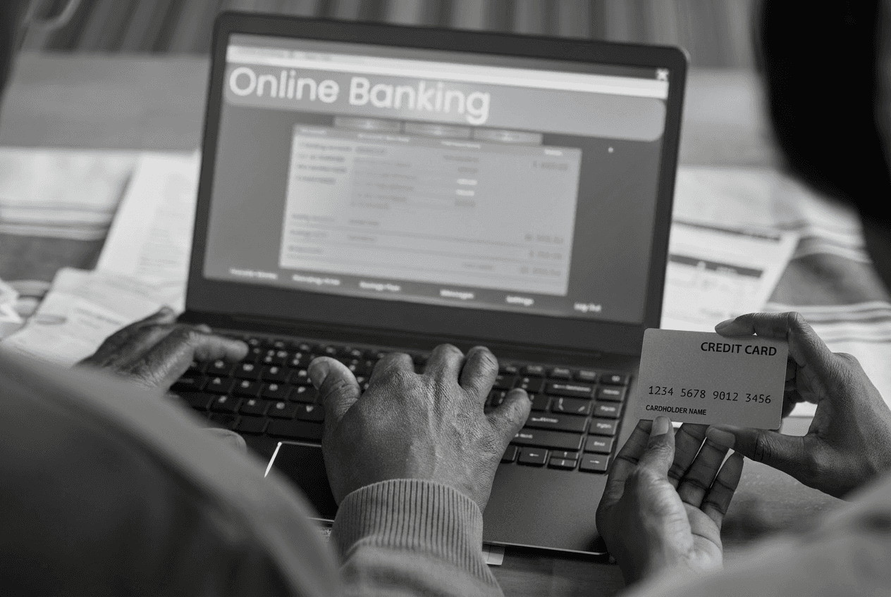 Two people using a laptop for online banking while one person holds a credit card, exposing the card details during the transaction