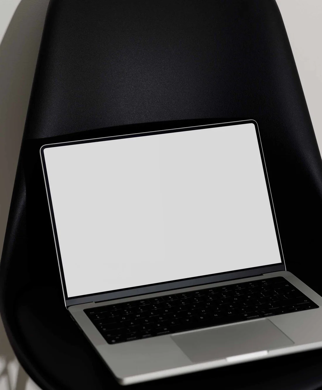 A silver MacBook with its screen displaying a minimalistic design against a gradient sunset background. The laptop is placed on a sleek black chair, creating a modern and elegant setup.