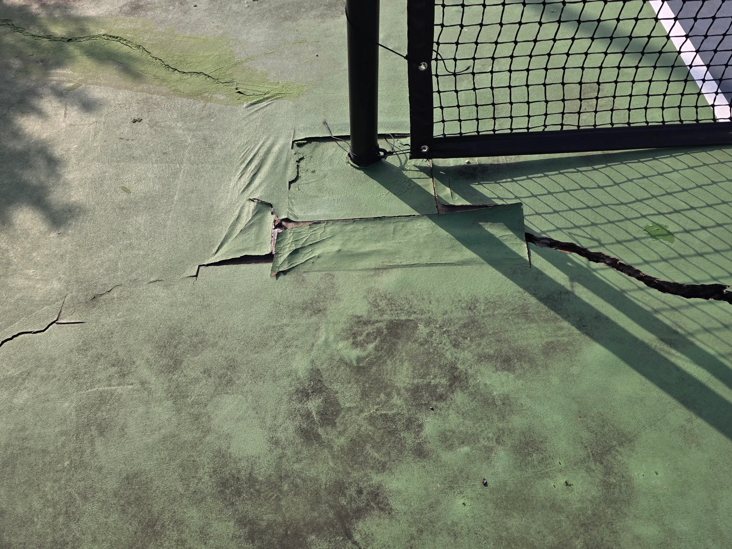 Cracked and peeling surface near the net post before resurfacing at Weston Ranch in Madison, AL
