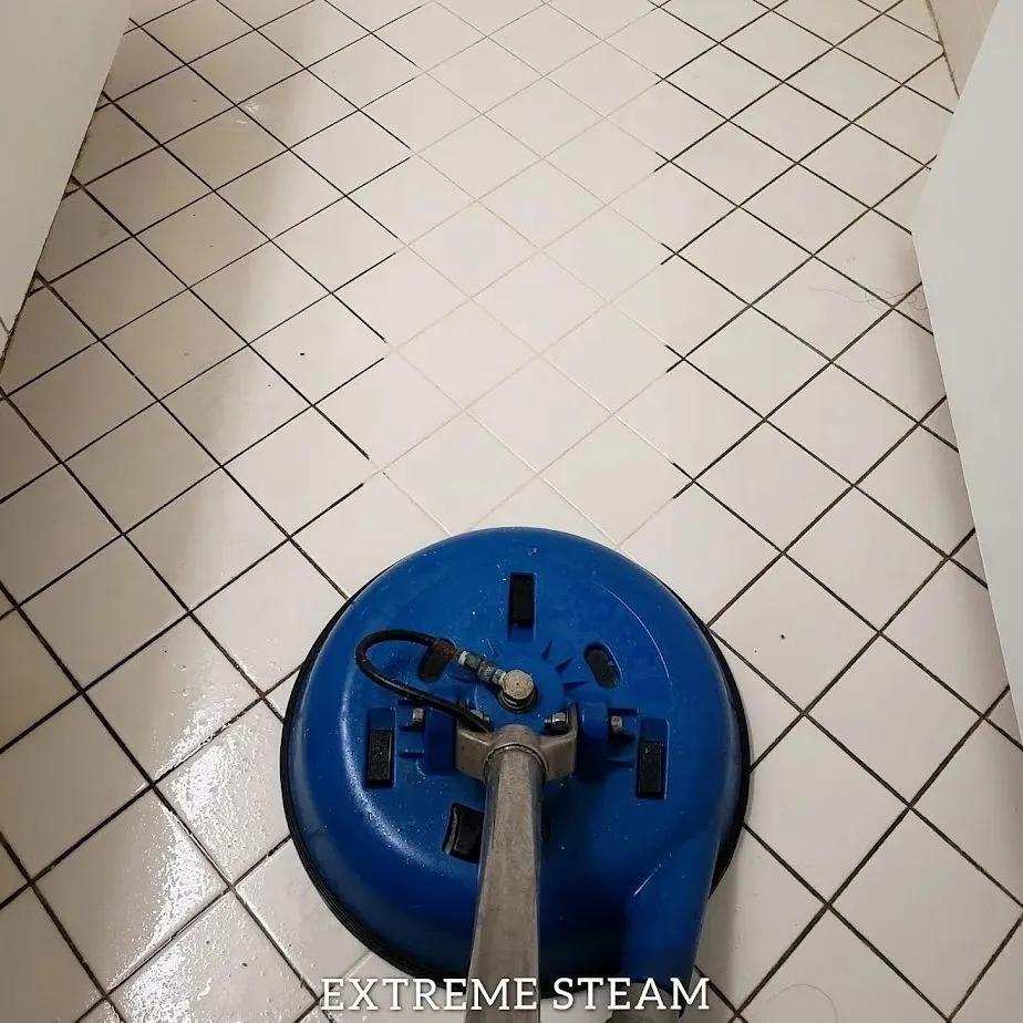 Tile floor being cleaned with a blue steam cleaning machine, showing a before and after comparison.