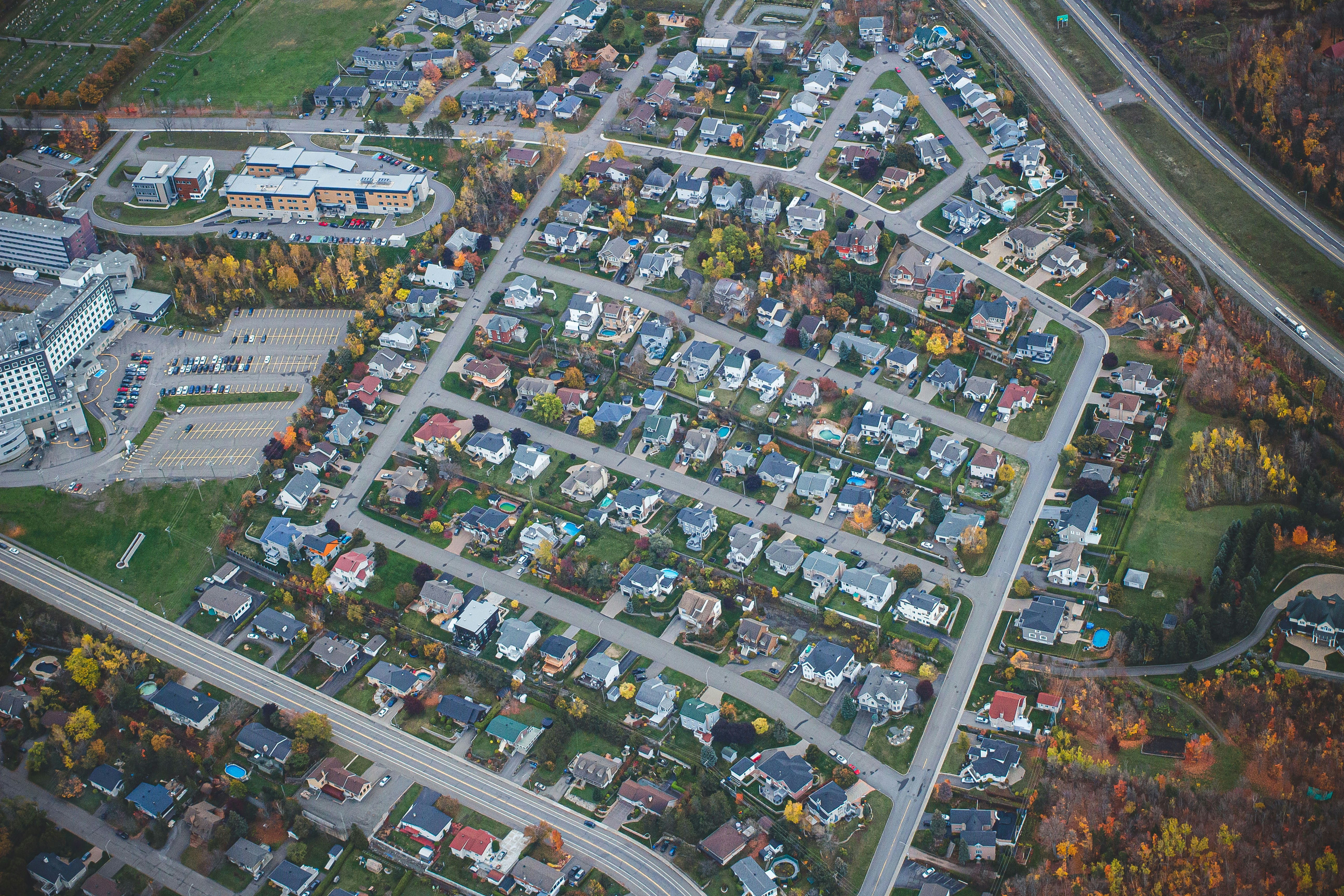 Aerial photograph of a sprawling suburban neighborhood with winding streets, detached homes, and autumn trees, illustrating the concept of a 'topical neighborhood' in AI-driven search engine optimization.