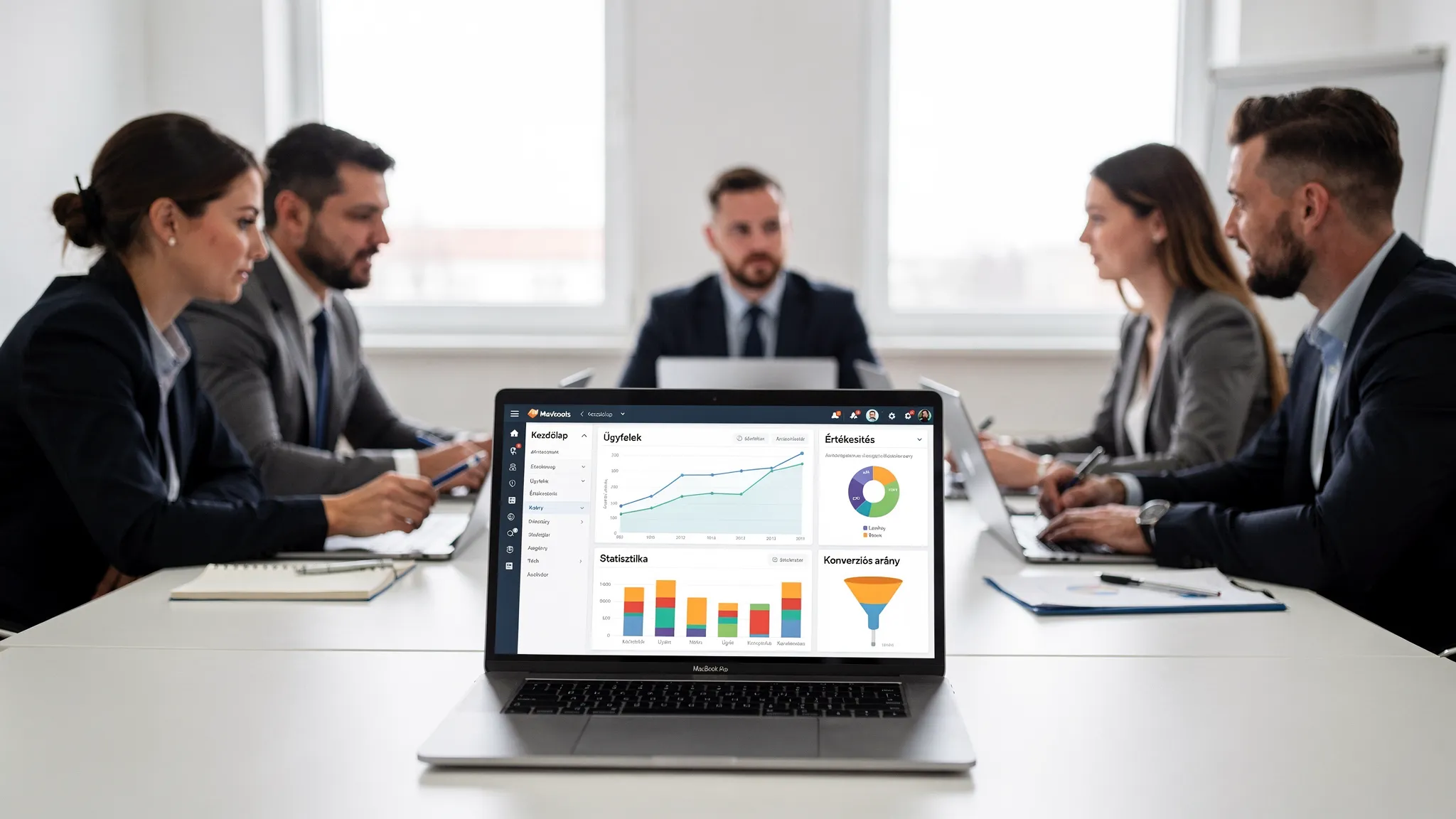 Egy magyar KKV csapat megbeszélést tart egy tárgyalóban, az asztalon laptopok vannak, a laptop képernyője a néző felé néz és egy egyszerű CRM dashboard grafikonjai látszanak rajta.
